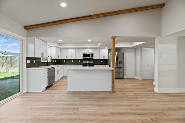 kitchen with a kitchen island, lofted ceiling, white cabinets, backsplash, and stainless steel appliances