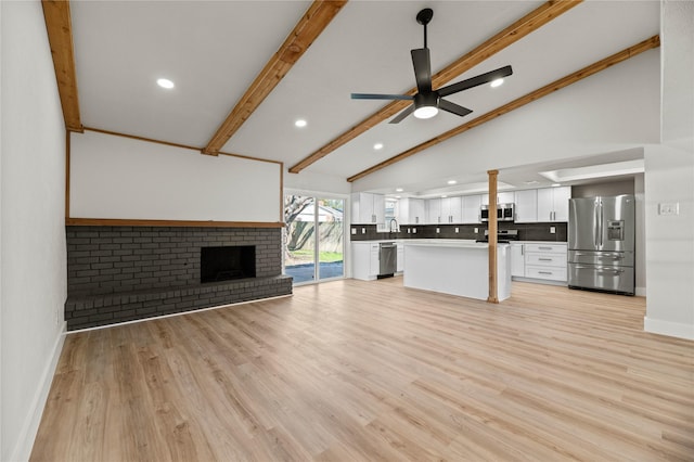 unfurnished living room featuring lofted ceiling with beams, sink, ceiling fan, a brick fireplace, and light wood-type flooring