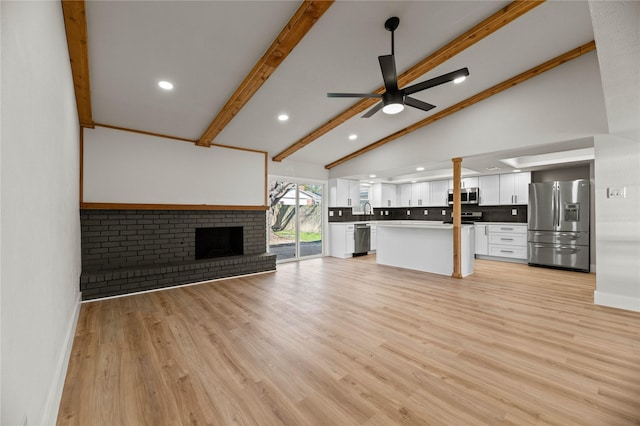 unfurnished living room featuring ceiling fan, a fireplace, light hardwood / wood-style floors, and vaulted ceiling with beams