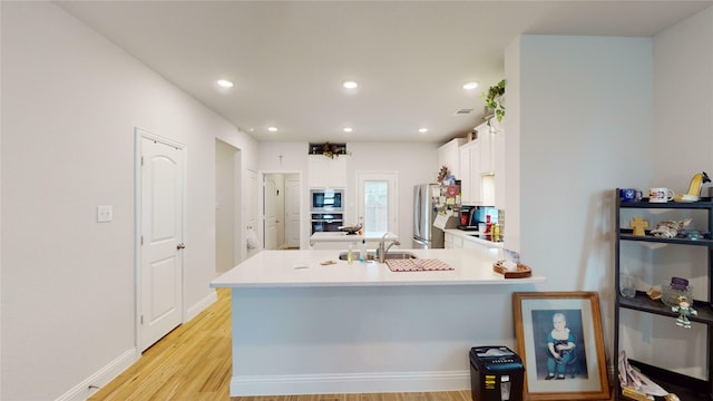 kitchen featuring built in microwave, sink, stainless steel fridge, kitchen peninsula, and white cabinets