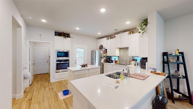 kitchen featuring sink, appliances with stainless steel finishes, kitchen peninsula, light hardwood / wood-style floors, and white cabinets