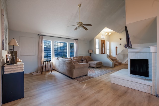 living room with vaulted ceiling, a brick fireplace, light hardwood / wood-style flooring, a textured ceiling, and ceiling fan with notable chandelier