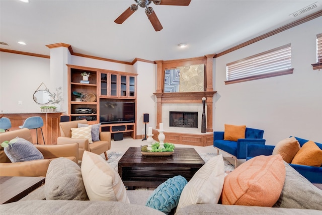 living room with a tile fireplace, ceiling fan, and crown molding