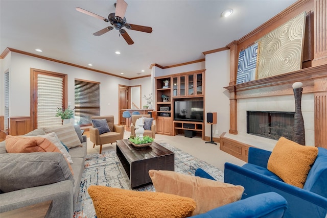 living room with a tiled fireplace, crown molding, ceiling fan, and carpet