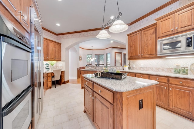 kitchen with hanging light fixtures, appliances with stainless steel finishes, a center island, and light stone counters