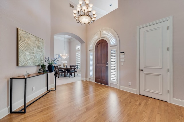 entrance foyer featuring an inviting chandelier, ornamental molding, a high ceiling, and light wood-type flooring