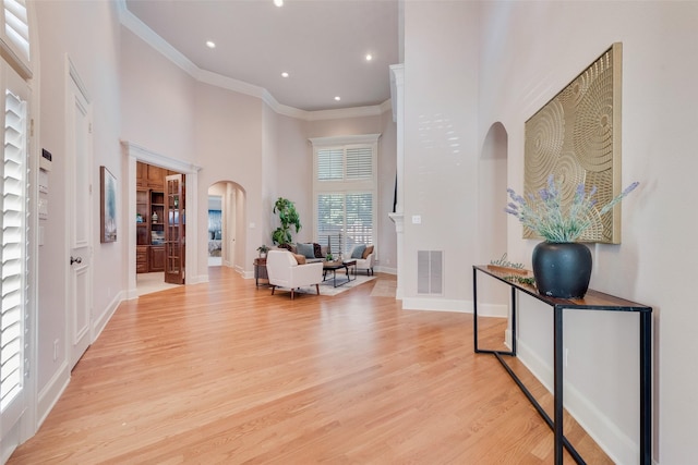 entryway with crown molding, light hardwood / wood-style floors, and a high ceiling