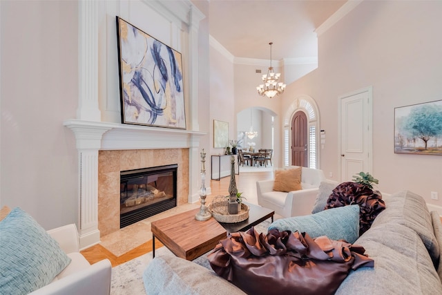 living room featuring a premium fireplace, crown molding, a towering ceiling, and a notable chandelier