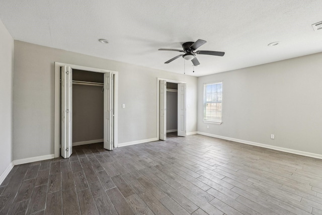 unfurnished bedroom featuring two closets, dark hardwood / wood-style floors, and a textured ceiling