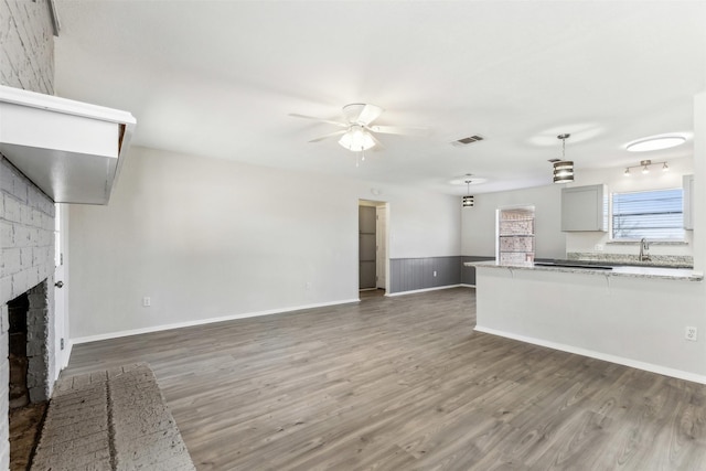 unfurnished living room with a brick fireplace, dark wood-type flooring, sink, and ceiling fan