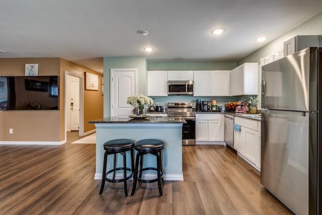 kitchen featuring white cabinetry, a center island, dark stone countertops, light wood-type flooring, and appliances with stainless steel finishes