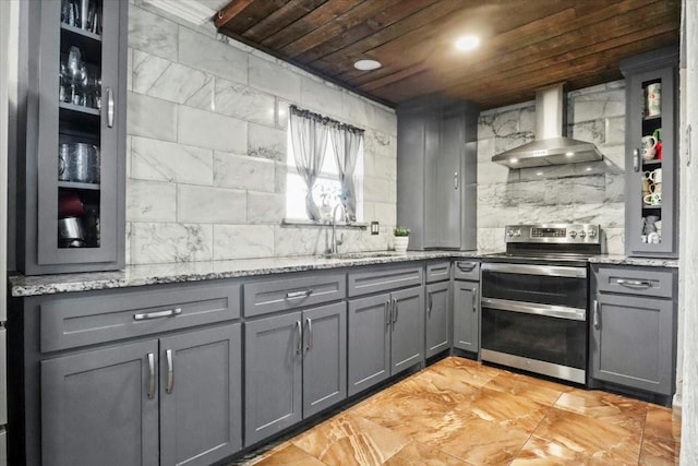 kitchen with sink, double oven range, gray cabinets, light stone countertops, and wall chimney range hood