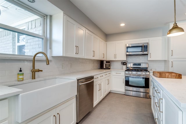 kitchen featuring light stone counters, hanging light fixtures, stainless steel appliances, and white cabinets