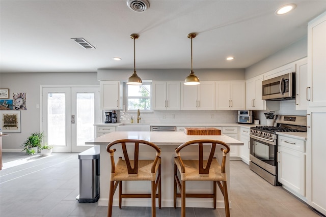 kitchen featuring appliances with stainless steel finishes, white cabinetry, sink, hanging light fixtures, and french doors