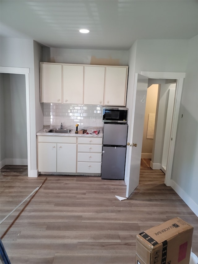 kitchen featuring appliances with stainless steel finishes, white cabinetry, sink, decorative backsplash, and light wood-type flooring