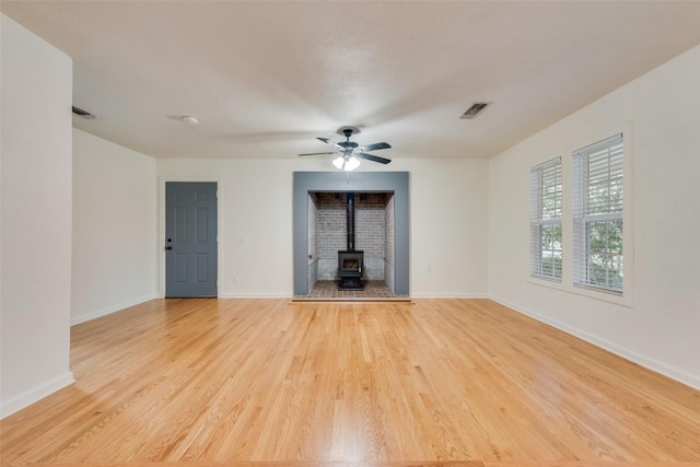 unfurnished living room featuring a wood stove, ceiling fan, and light hardwood / wood-style flooring