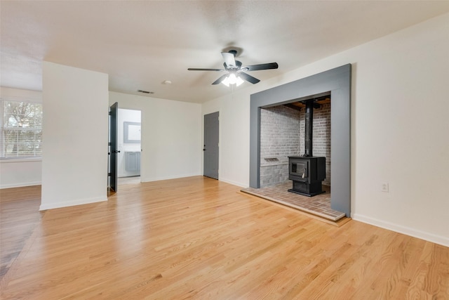 unfurnished living room with light hardwood / wood-style flooring, ceiling fan, and a wood stove