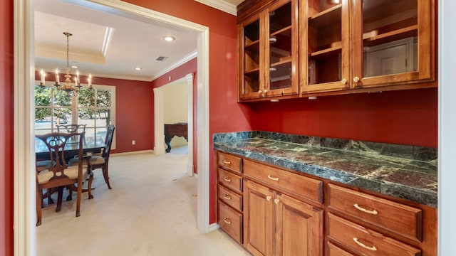 kitchen featuring dark stone countertops, hanging light fixtures, ornamental molding, a notable chandelier, and light carpet