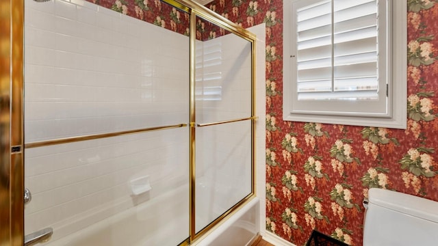 bathroom featuring toilet and shower / bath combination with glass door