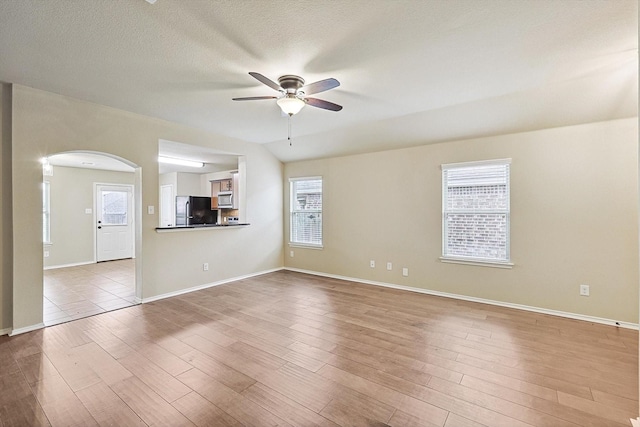 spare room featuring ceiling fan, vaulted ceiling, a textured ceiling, and light wood-type flooring