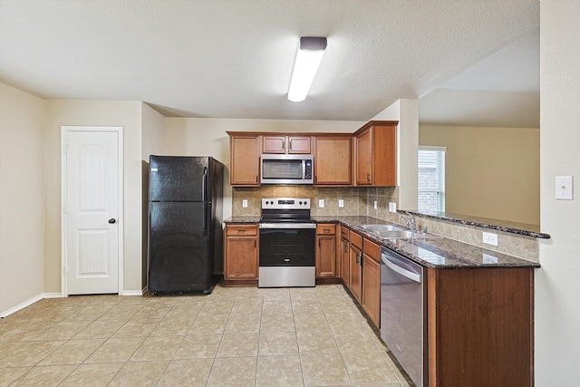 kitchen with light tile patterned floors, appliances with stainless steel finishes, dark stone countertops, decorative backsplash, and kitchen peninsula