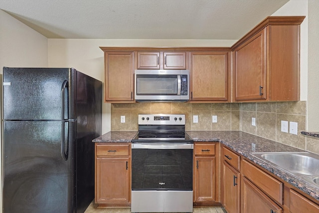 kitchen featuring appliances with stainless steel finishes, sink, dark stone countertops, backsplash, and a textured ceiling