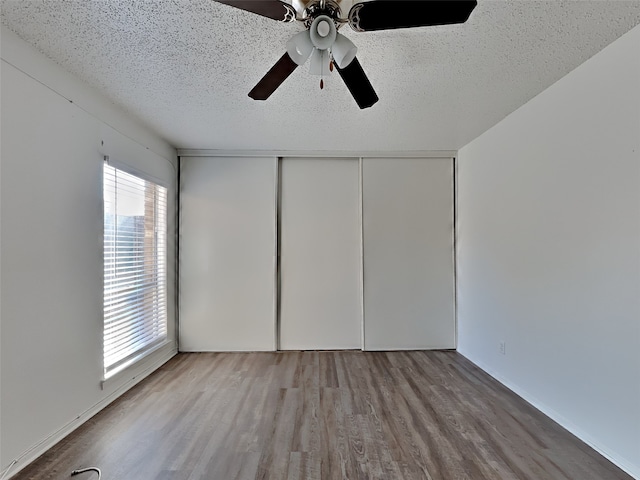 unfurnished bedroom with ceiling fan, a closet, wood-type flooring, and a textured ceiling