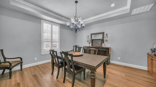 dining space featuring crown molding, a tray ceiling, a chandelier, and light hardwood / wood-style floors