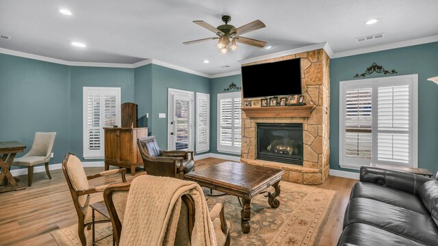 living room with crown molding, ceiling fan, a fireplace, and light wood-type flooring