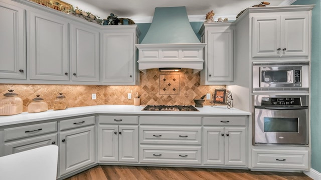 kitchen with light hardwood / wood-style flooring, white cabinetry, stainless steel appliances, decorative backsplash, and custom exhaust hood