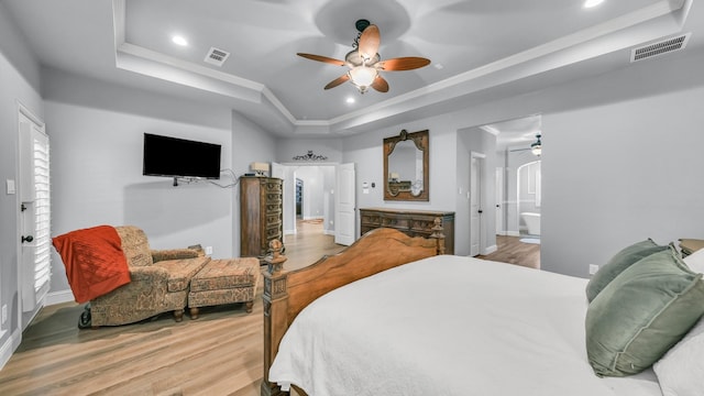 bedroom with ornamental molding, a tray ceiling, ensuite bathroom, and light hardwood / wood-style flooring