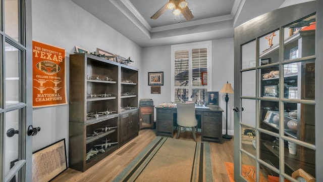 office space featuring ornamental molding, ceiling fan, light wood-type flooring, and a tray ceiling