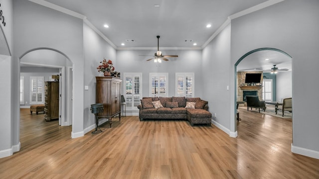 living room featuring a stone fireplace, light hardwood / wood-style floors, ceiling fan, and a towering ceiling