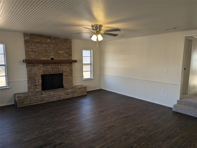 unfurnished living room featuring ceiling fan, dark hardwood / wood-style flooring, and a stone fireplace