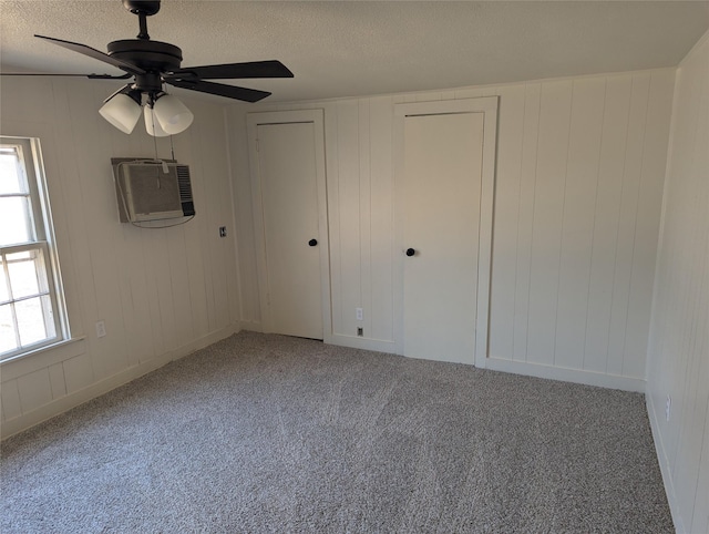 unfurnished bedroom with ceiling fan, a wall unit AC, carpet floors, and a textured ceiling