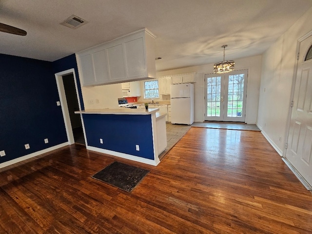 kitchen with dark hardwood / wood-style floors, kitchen peninsula, white fridge, and white cabinets