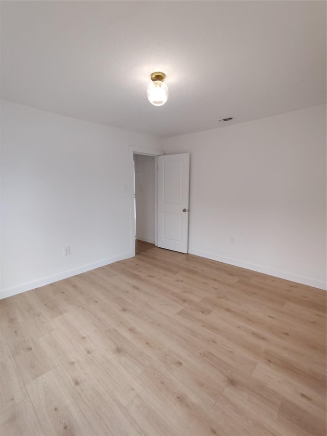 spare room featuring light wood finished floors, visible vents, and baseboards