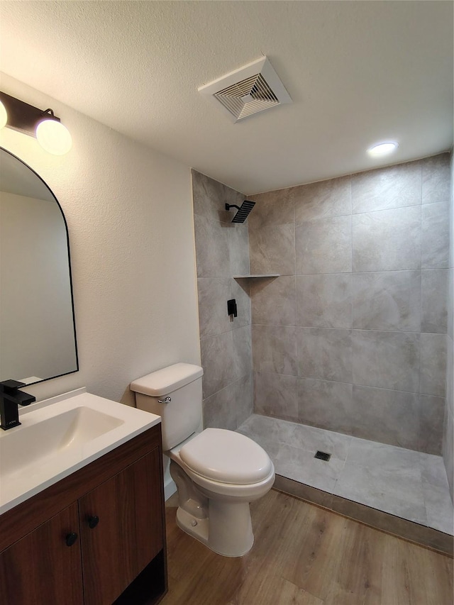 full bath featuring visible vents, toilet, wood finished floors, a tile shower, and vanity