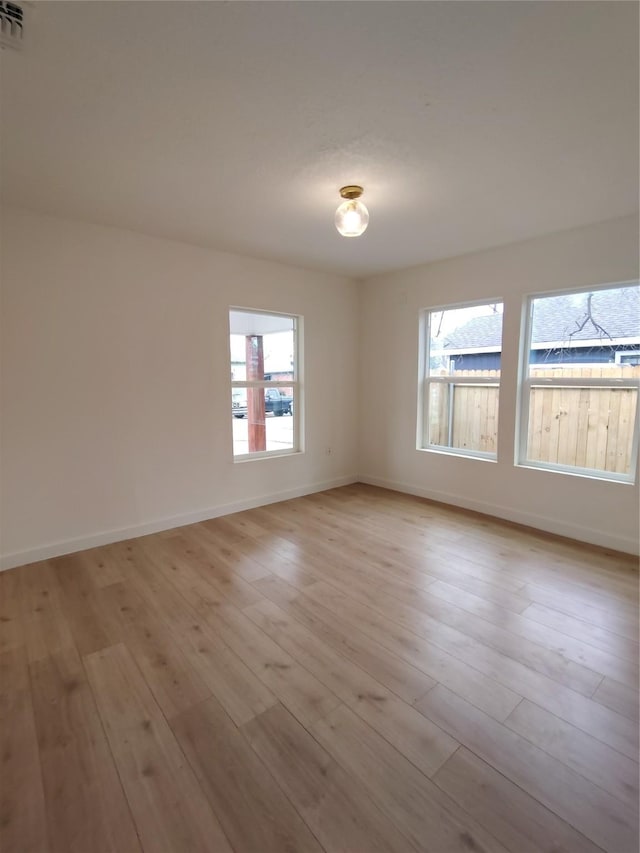 unfurnished room with light wood-type flooring, a wealth of natural light, and baseboards