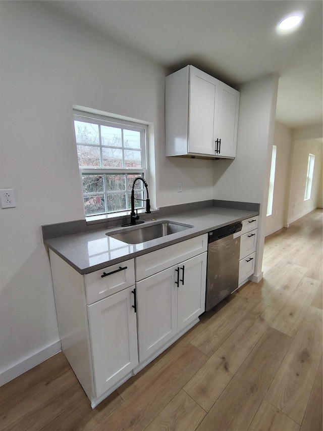 kitchen featuring light wood-style floors, white cabinets, a sink, dishwasher, and baseboards