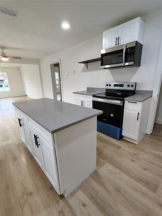 kitchen featuring a center island, range with electric stovetop, stainless steel microwave, visible vents, and light wood-type flooring