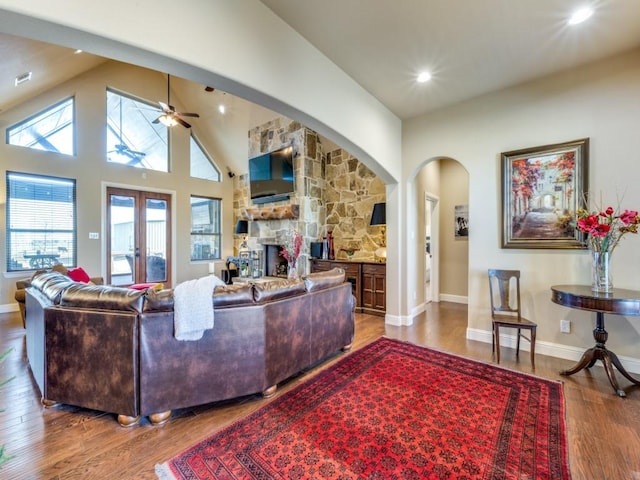 living room with ceiling fan, high vaulted ceiling, a fireplace, wood-type flooring, and french doors