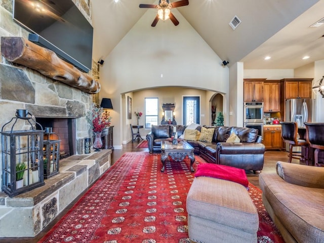 living room with ceiling fan, wood-type flooring, a stone fireplace, and high vaulted ceiling