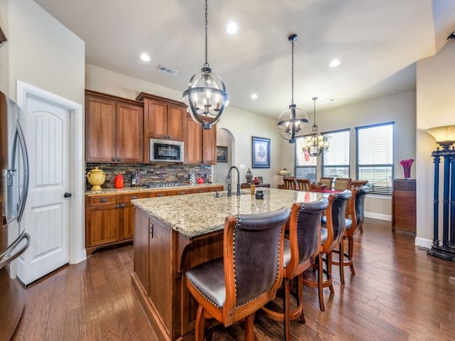 kitchen featuring appliances with stainless steel finishes, a kitchen breakfast bar, dark hardwood / wood-style floors, a center island with sink, and decorative light fixtures