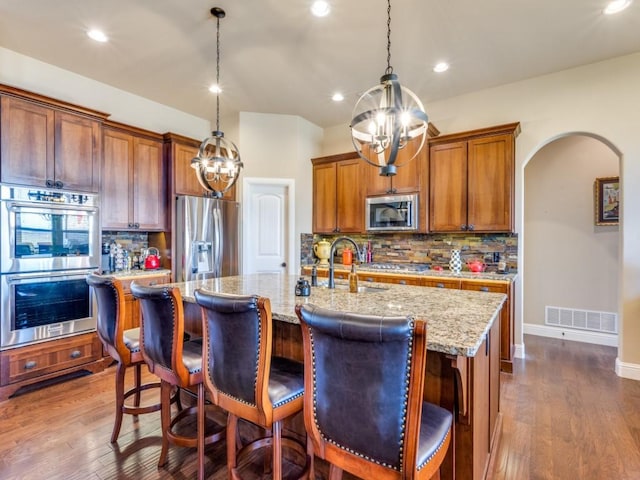 kitchen featuring stainless steel appliances, sink, a kitchen island with sink, and hanging light fixtures