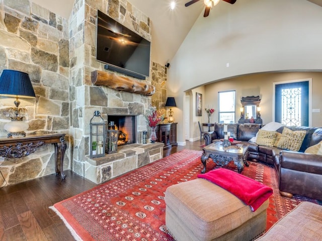 living room featuring a stone fireplace, high vaulted ceiling, dark hardwood / wood-style floors, and ceiling fan