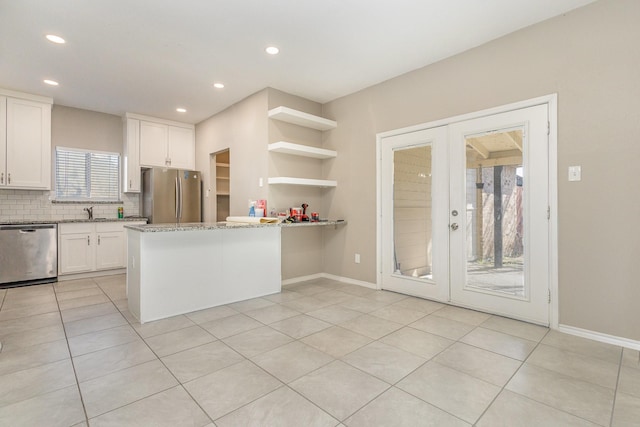 kitchen with appliances with stainless steel finishes, white cabinetry, light stone countertops, kitchen peninsula, and french doors