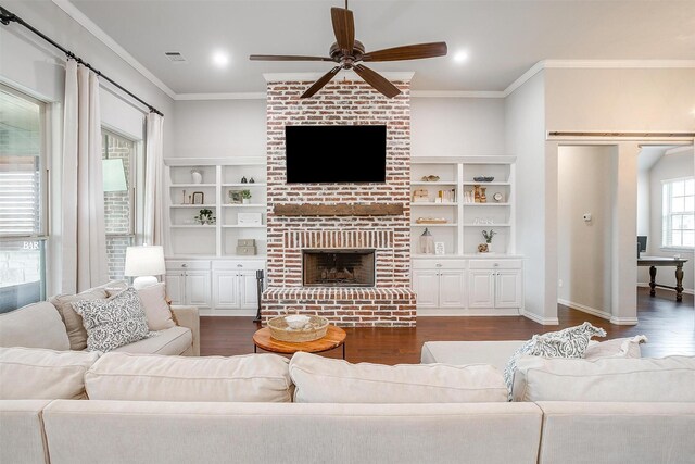 living room featuring built in shelves, crown molding, a brick fireplace, dark hardwood / wood-style flooring, and ceiling fan