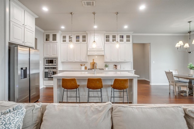 kitchen with appliances with stainless steel finishes, white cabinetry, an island with sink, a kitchen bar, and decorative light fixtures