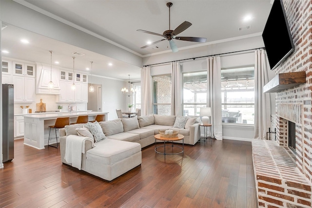 living room with crown molding, ceiling fan with notable chandelier, a fireplace, and dark hardwood / wood-style flooring